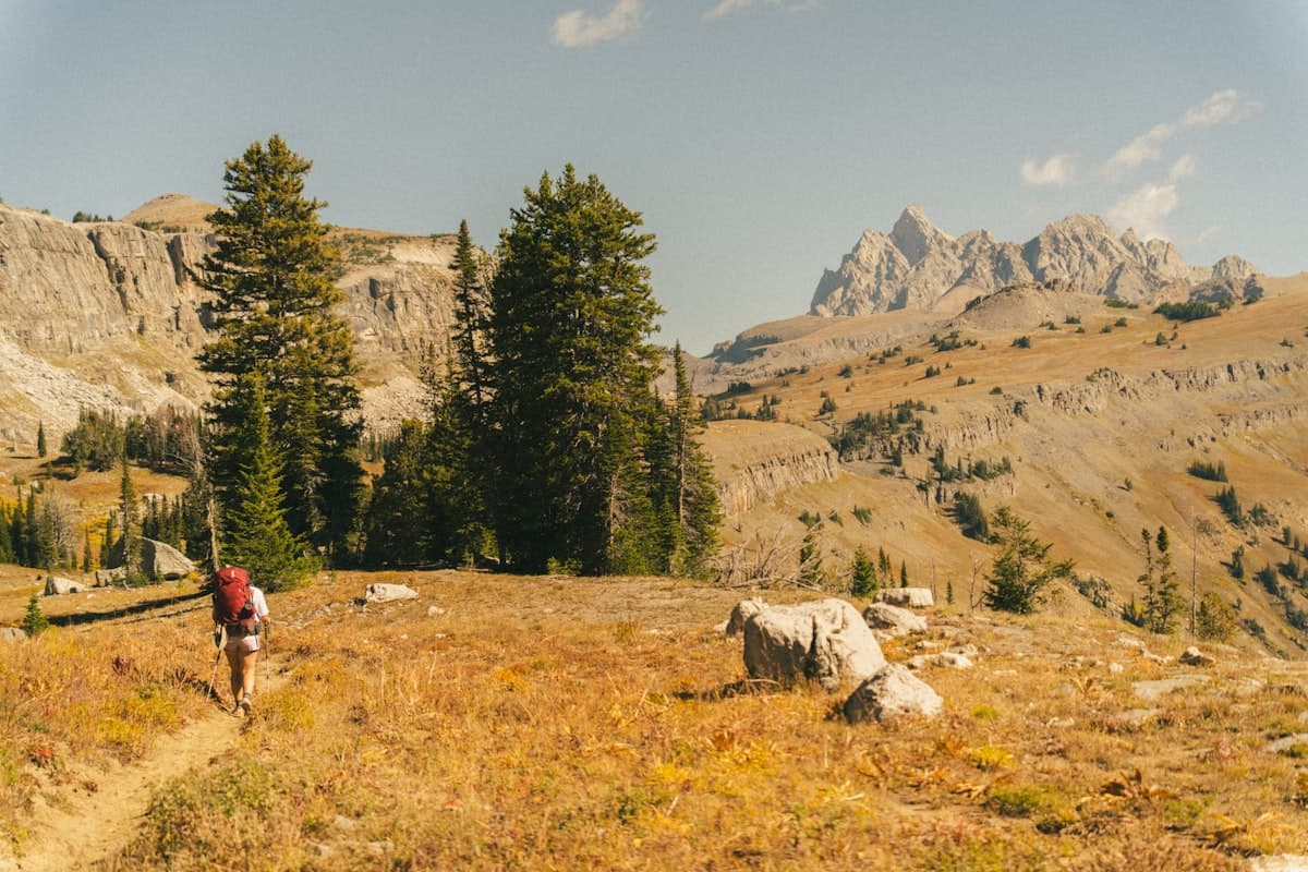 A hiker with a loaded backpack walking on a mountain trail in rugged terrain