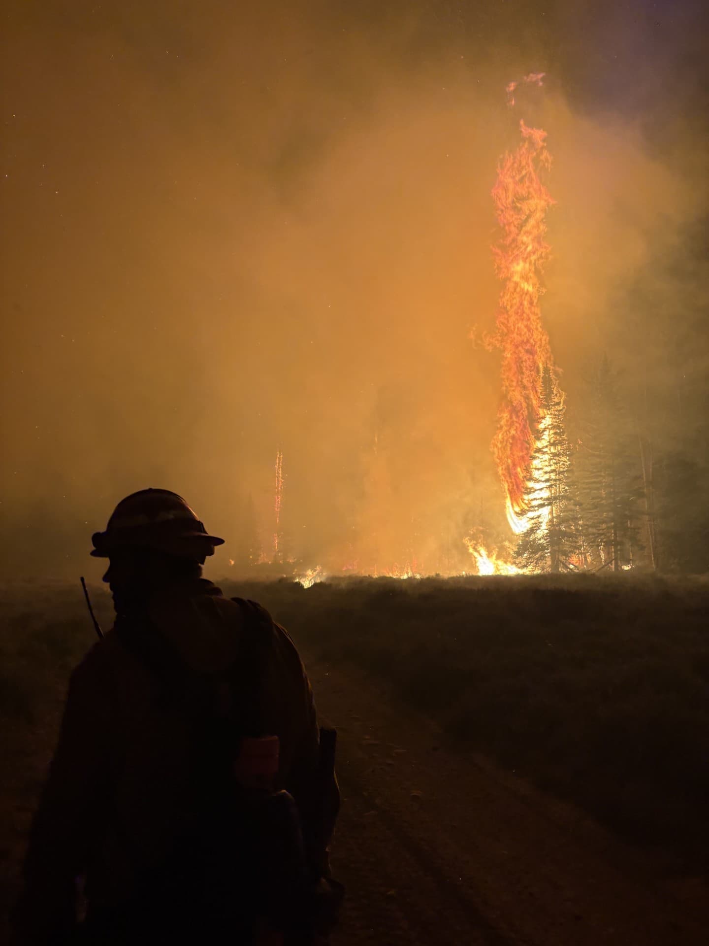 Wildland firefighter silhouetted against flames during night operations